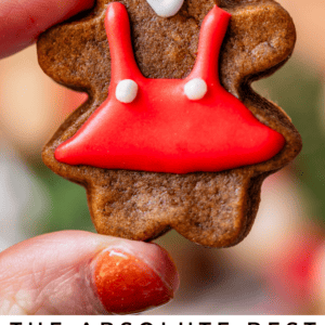 girl gingerbread cookie with red dress, held up by fingers.
