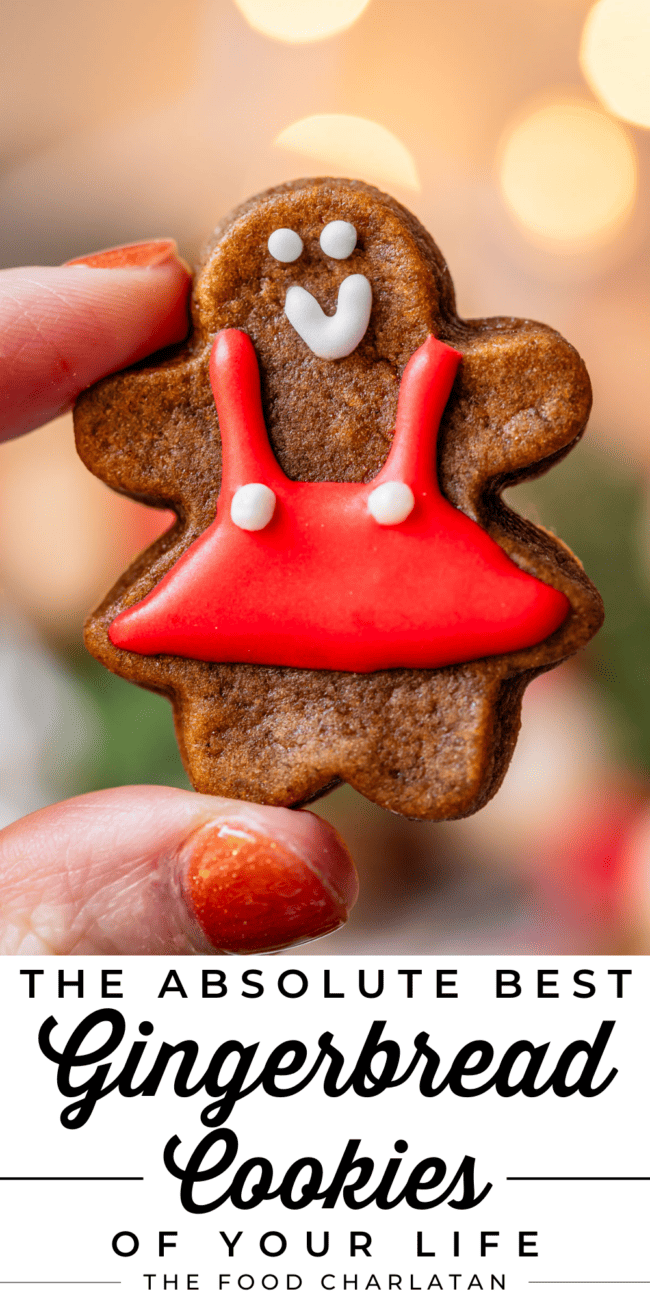 girl gingerbread cookie with red dress, held up by fingers.