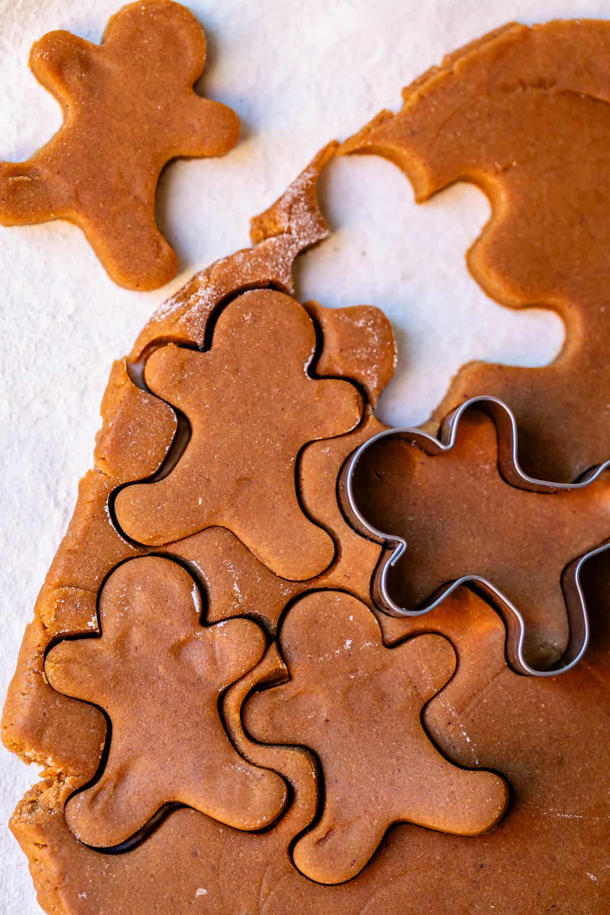 a rolled out section of gingerbread cookie dough with cookie cutters about to cut through the dough.