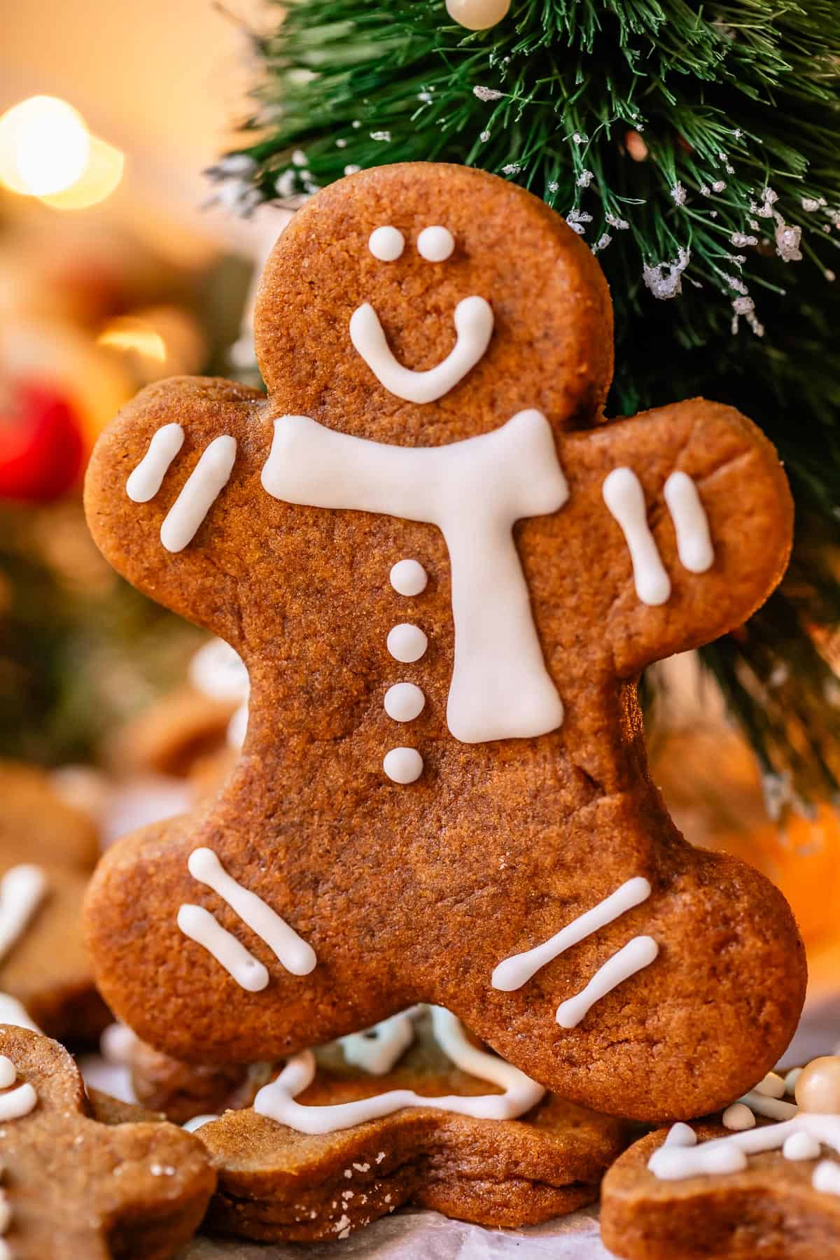 gingerbread man cookie with white icing propped up against a christmas tree.
