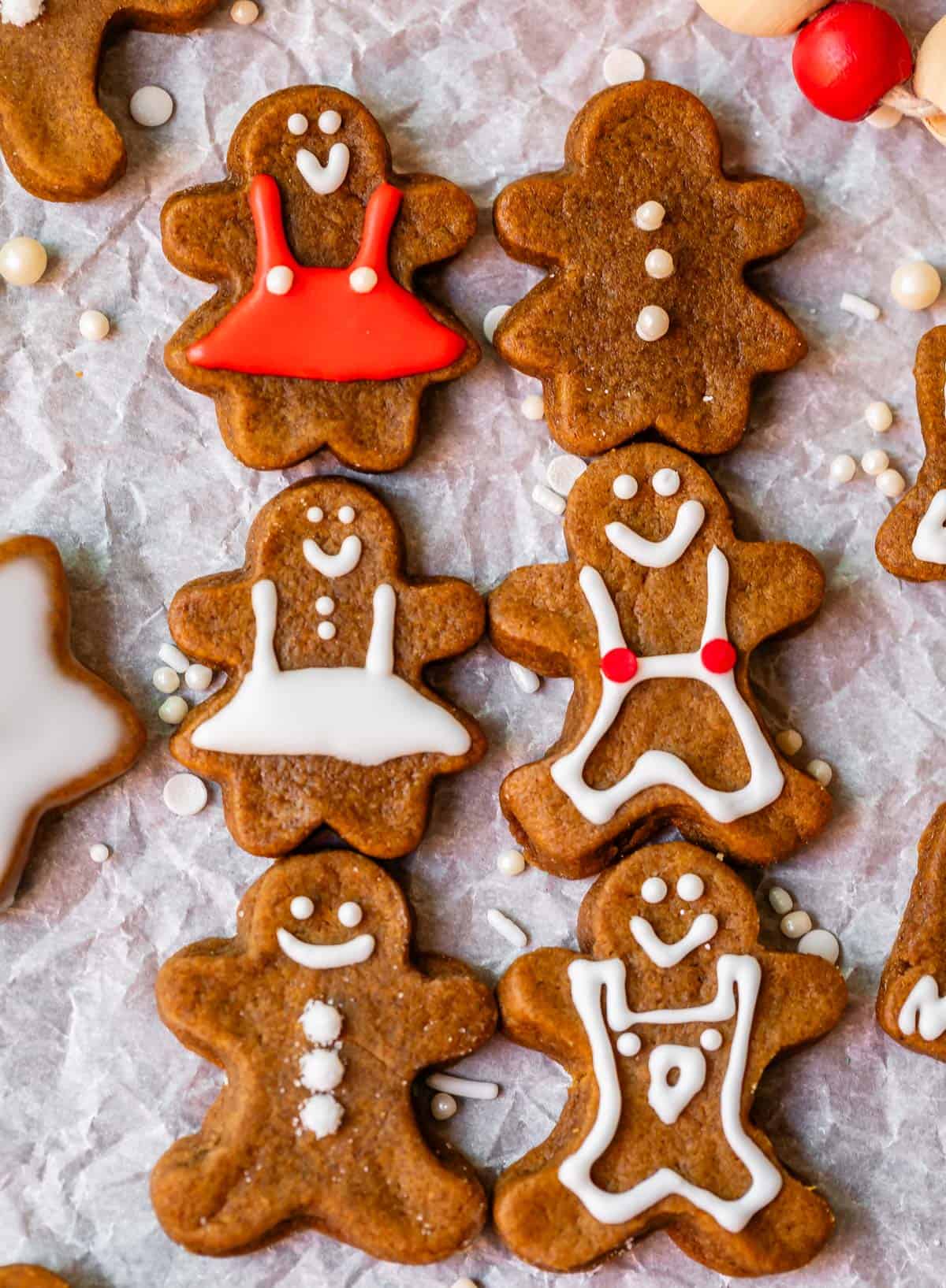 6 gingerbread people with white and red icing lined up on parchment paper.
