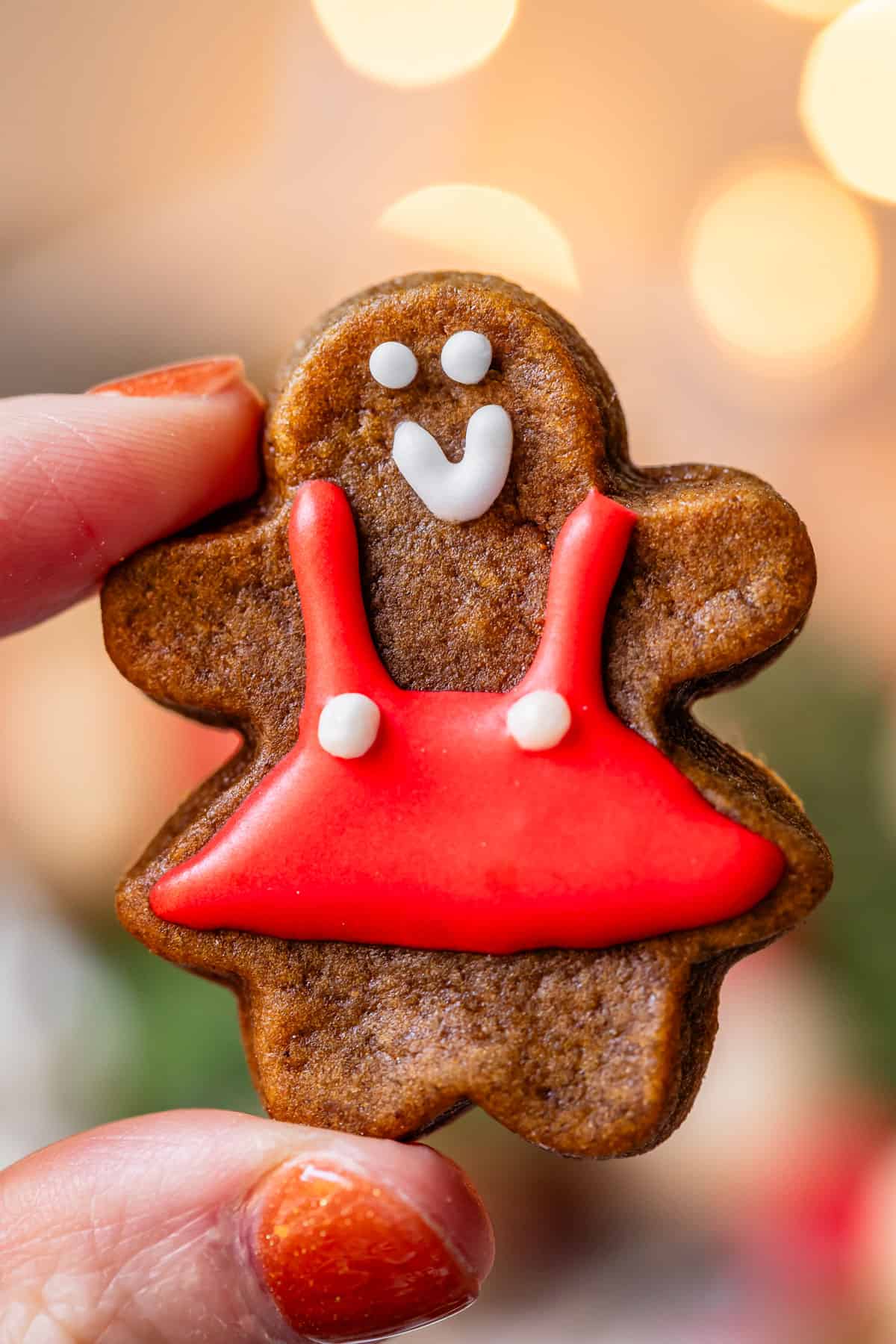 hand holding up tiny gingerbread cookie with red dress.