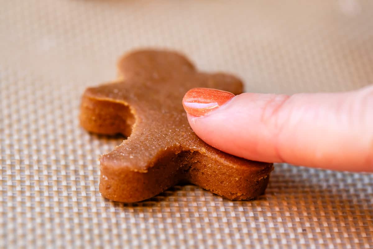 a tiny 2" cut out gingerbread man on a silpat with a finger brushing flour off the sides.