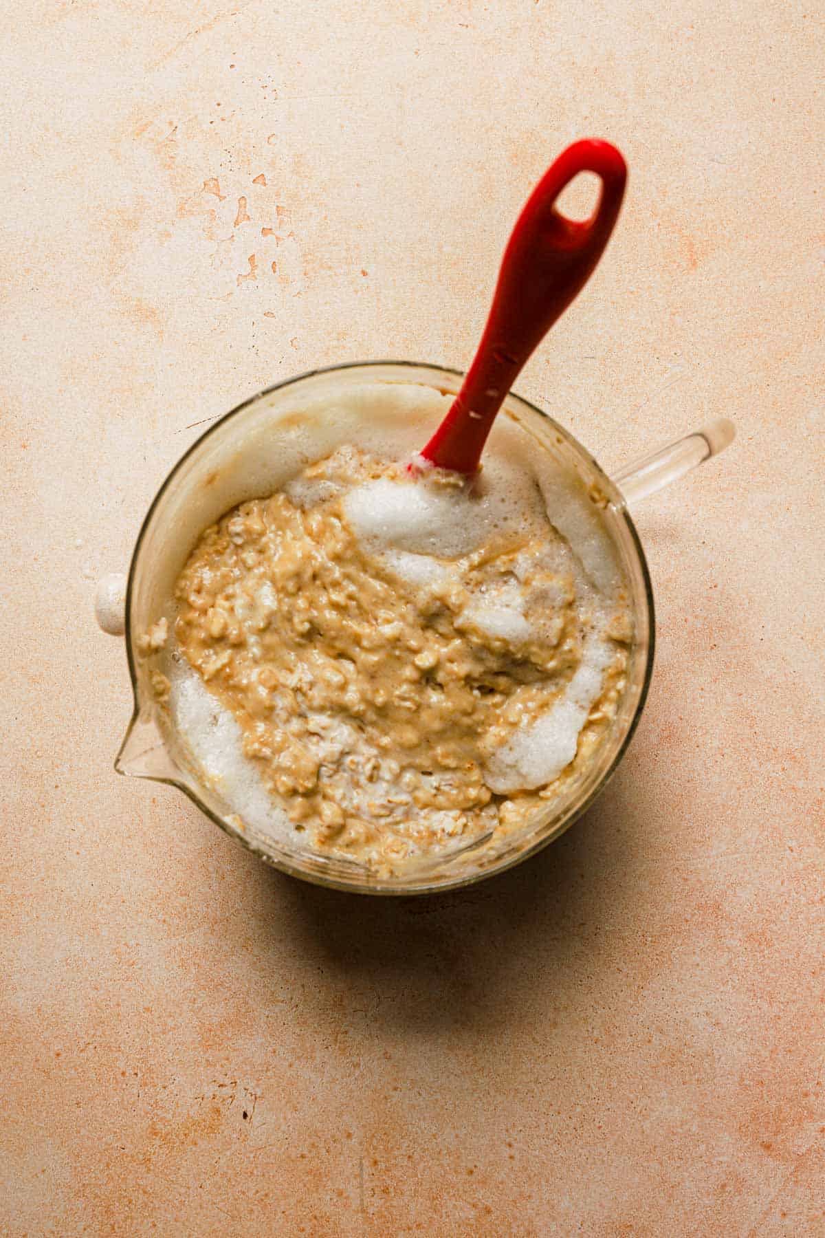 Mixing beaten egg whites into oatmeal pancake batter in large glass measuring bowl with spatula.