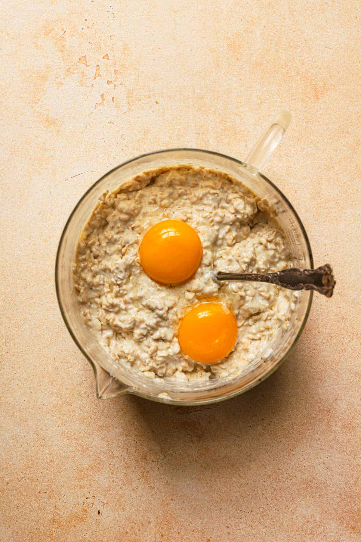 Soaked oats with eggs on top from above ready to be mixed in large measuring cup.