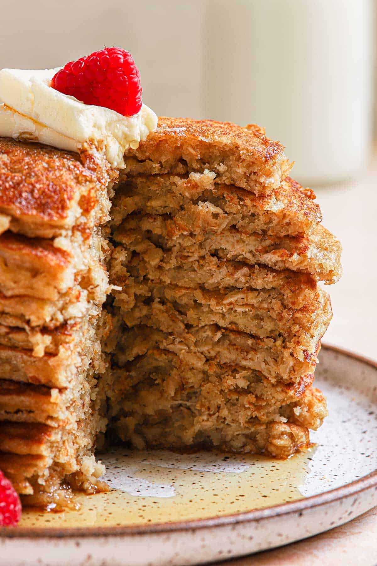 Tall stack of oatmeal pancakes with a quarter cut out covered in butter and syrup.