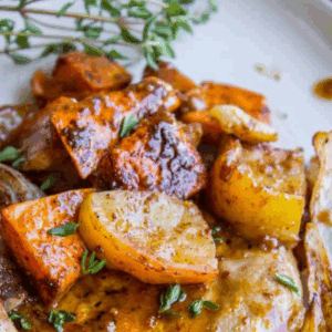 A plate with pan seared pork chops in apple cider, roasted sweet potatoes, apple slices, and herbs, covered in sauce. The text above reads: “Apple Cider Pork Chop Dinner – The Food Charlatan.”.