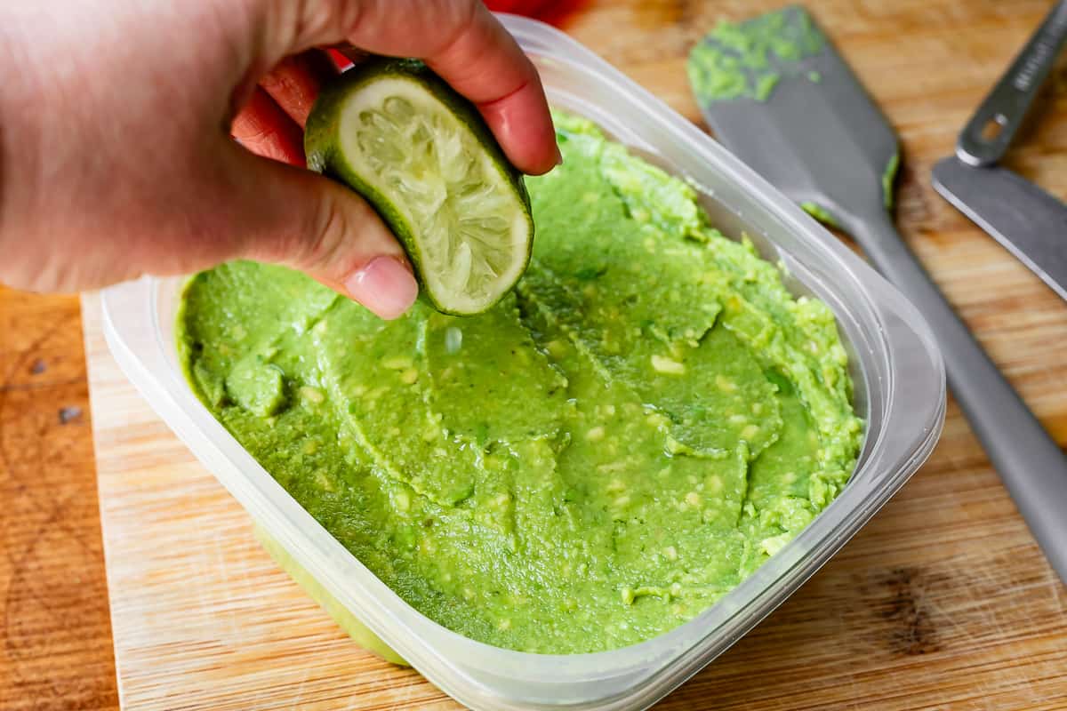 half a lime squeezing juice over the smoothed top of guacamole in a tupperware.