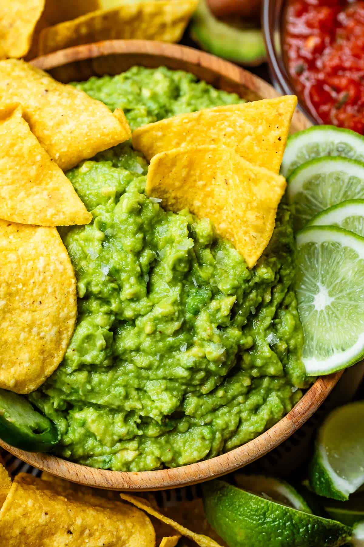 close up of a wooden bowl with guacamole in it with chips dipped into the guac.