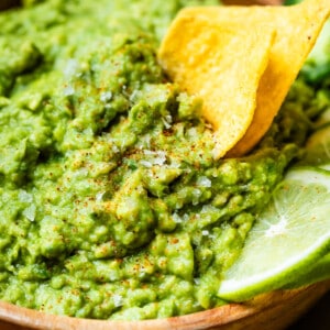 close up showing detail of guacamole with flakes of salt and 2 chips perfectly scooping into it.