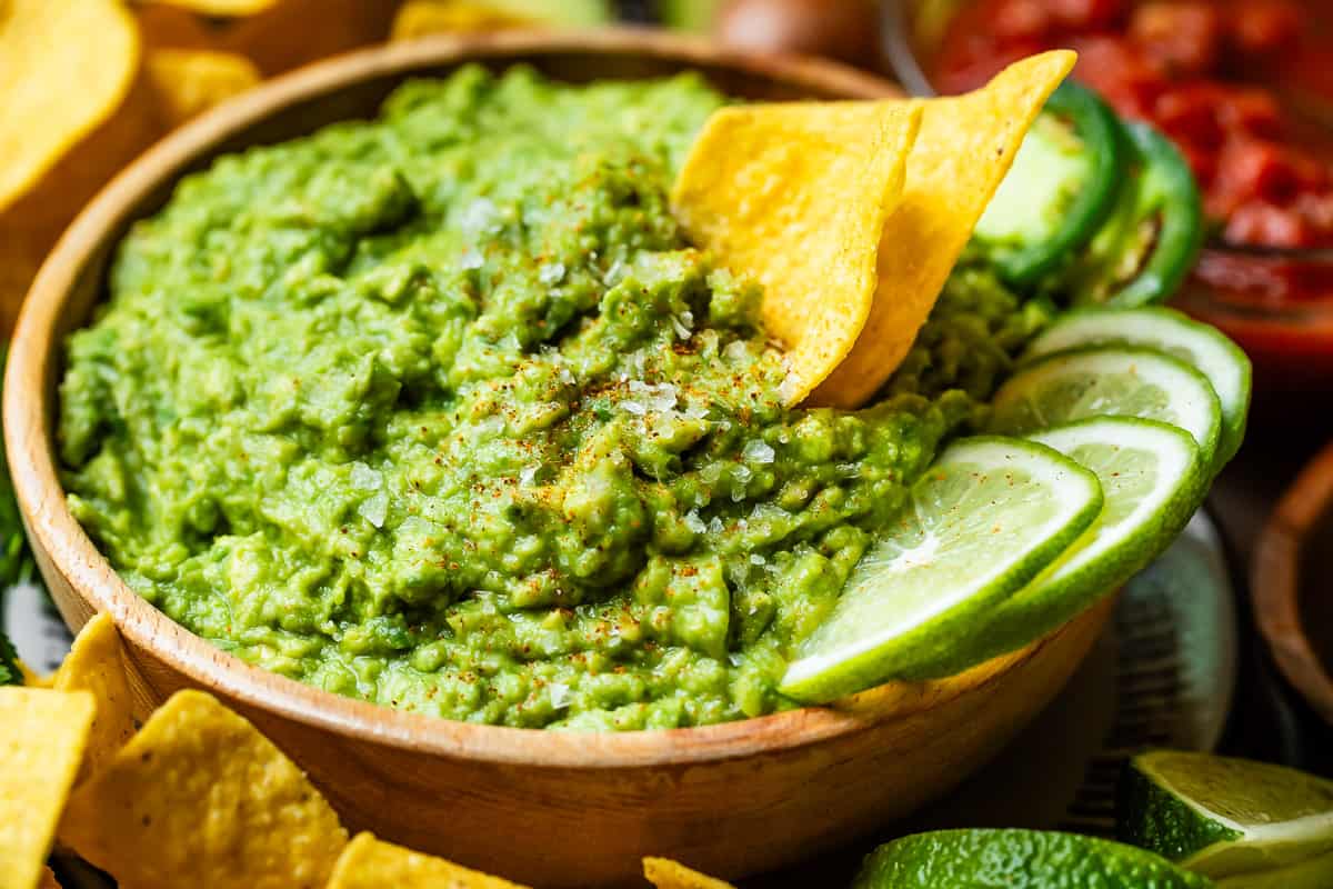 close up showing the chunky texture of guacamole with lime and chips as garnish.