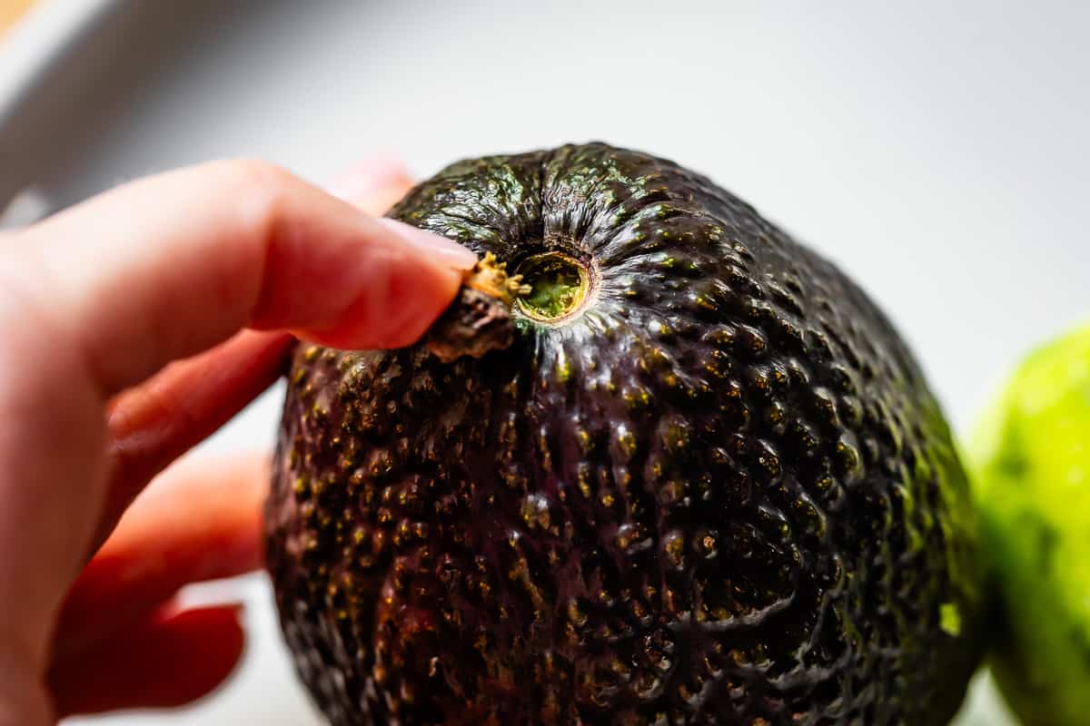 finger removing the stem at the top of an avocado to show green which means it's ripe.