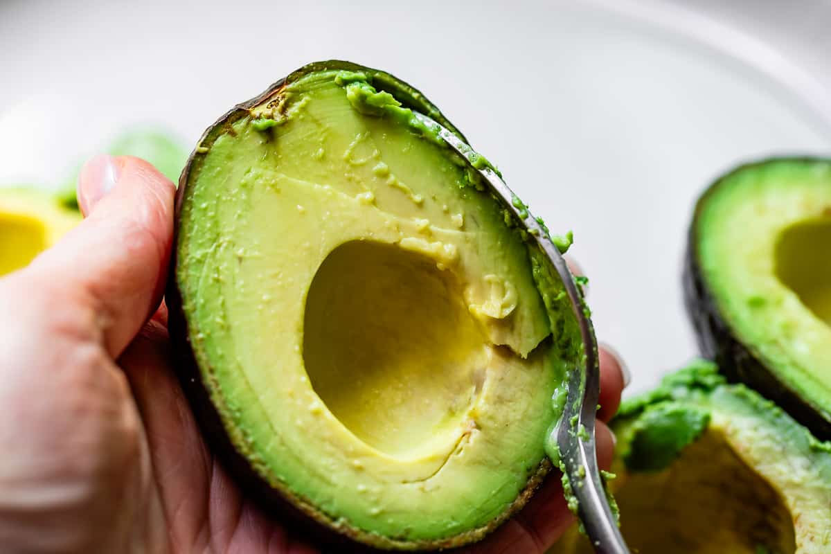 a spoon scraping along the inside of the avocado peel to scoop out all the flesh.