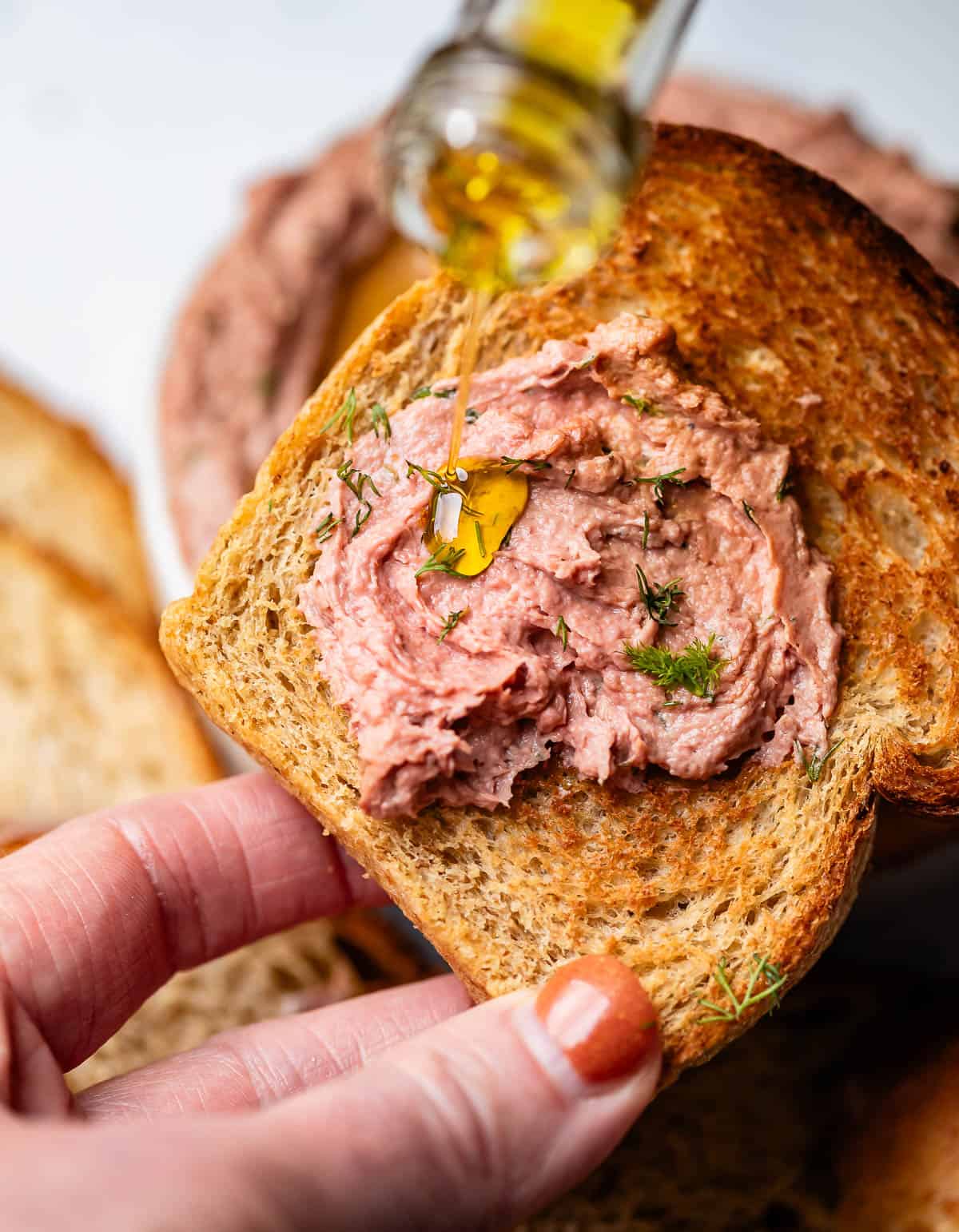 liver pate on toasted rye bread while pouring on olive oil.