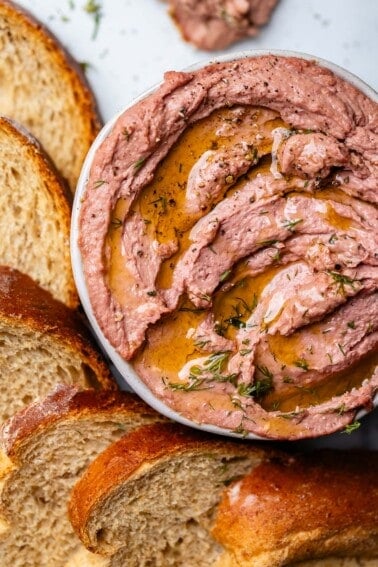 Liver pate in bowl surrounded by slices of rye bread.