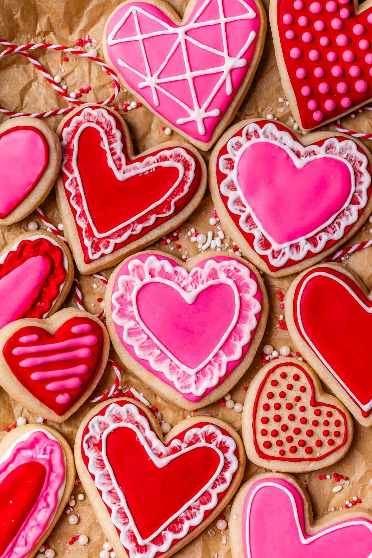 overhead shot of red and pink heart sugar cookies on parchment paper, frosted with royal icing.