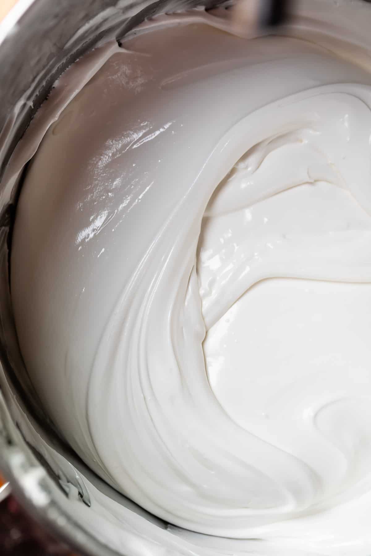 white toothpaste like consistency icing in a metal kitchen aid mixing bowl.