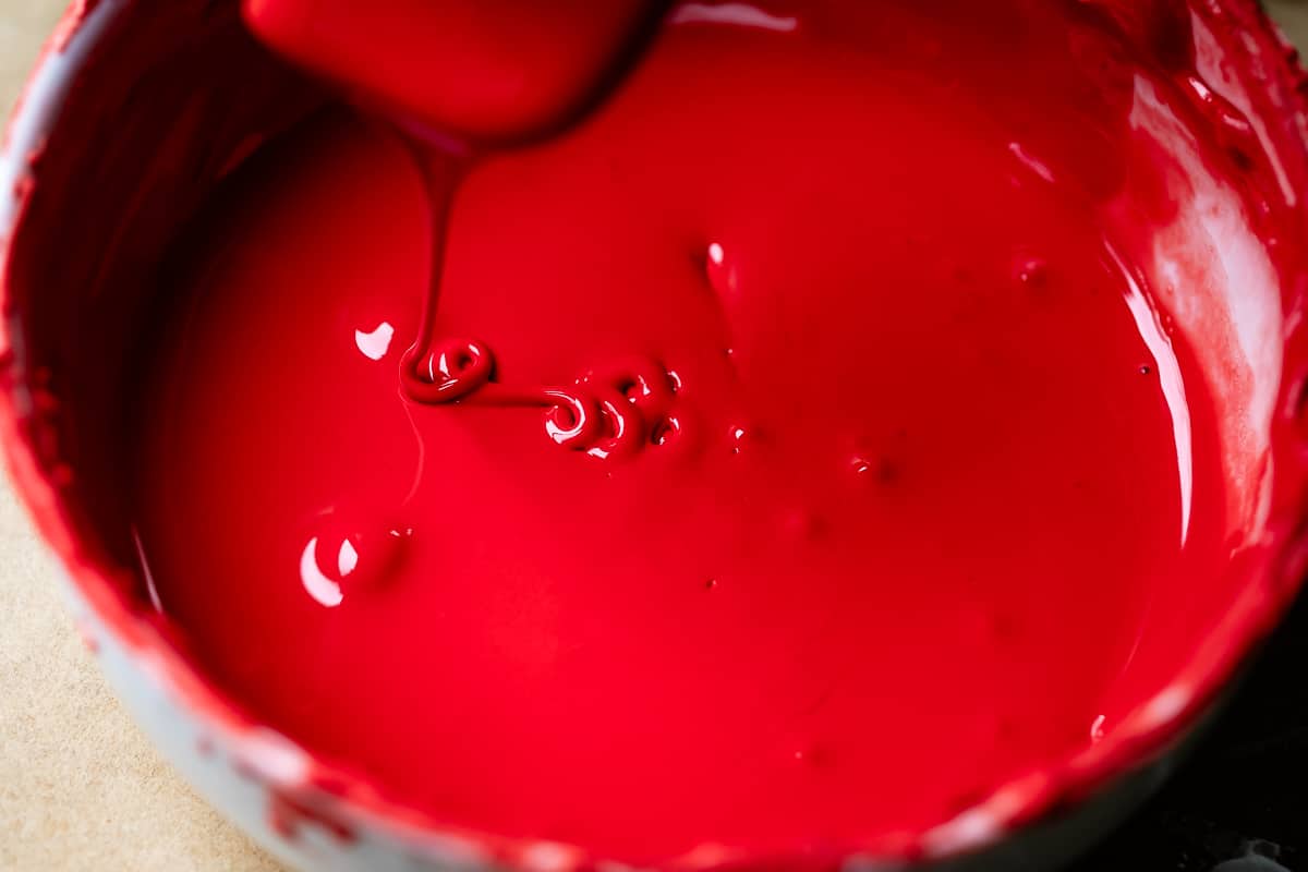 bowl of completely mixed in red frosting, dripping off a spoon into the bowl.