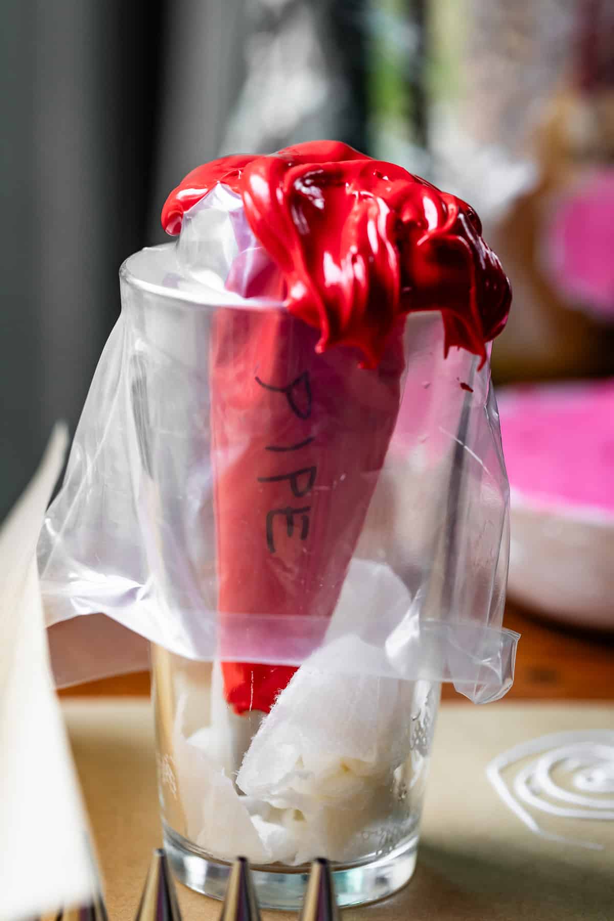 decorating bag with word "pipe" on it filled with red royal icing in a tall cup.