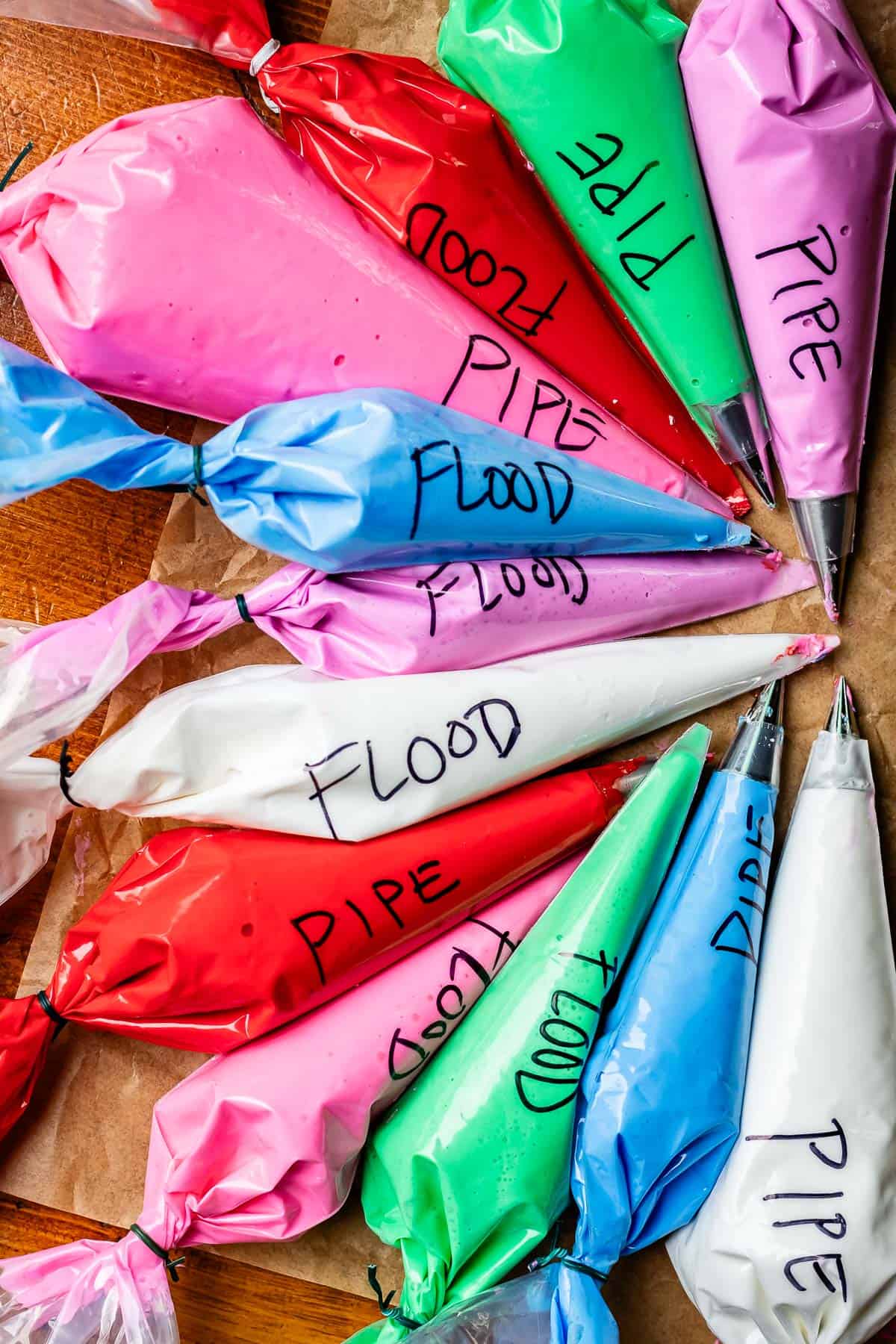 several piping bags filled with various colors of icing, with either pipe or flood written on the side.