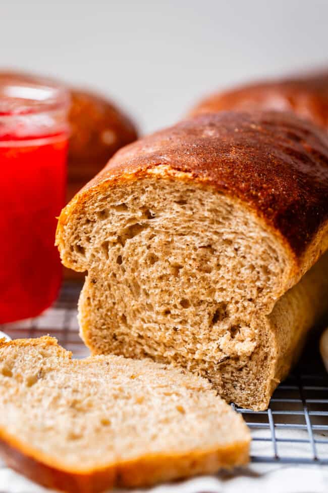 rye bead with a slice cut off with red jam in the background.