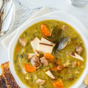 A bowl of split pea and ham soup garnished with bay leaves, served with slices of toasted bread.