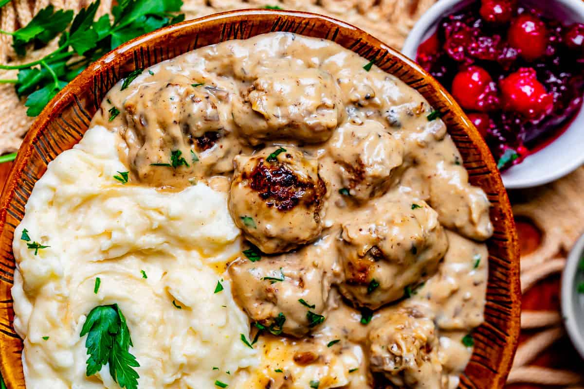 a ceramic bowl with a serving of mashed potatoes and swedish meatballs with brown sauce.