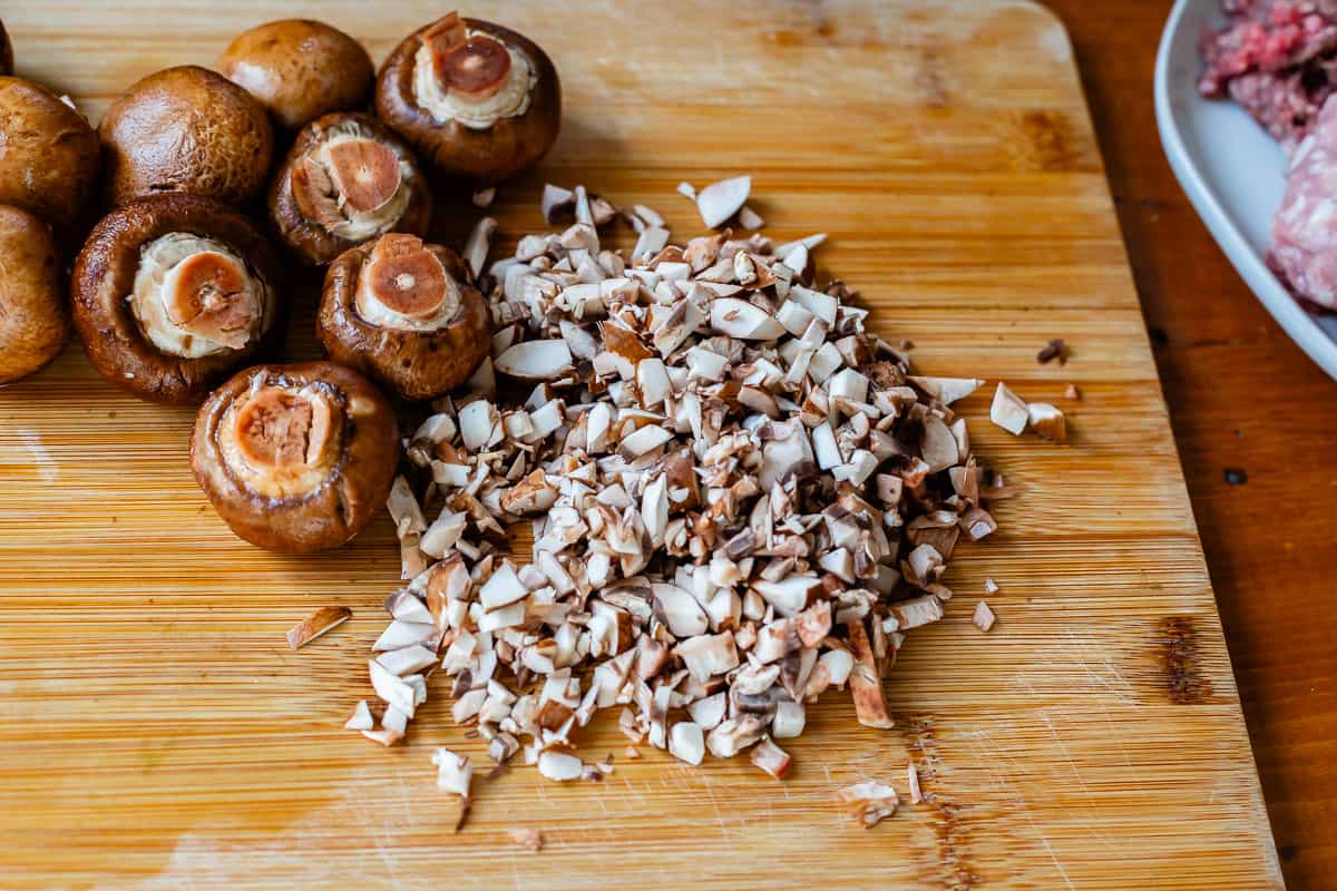 finely chopped mushrooms on a cutting board with whole mushrooms in the background.