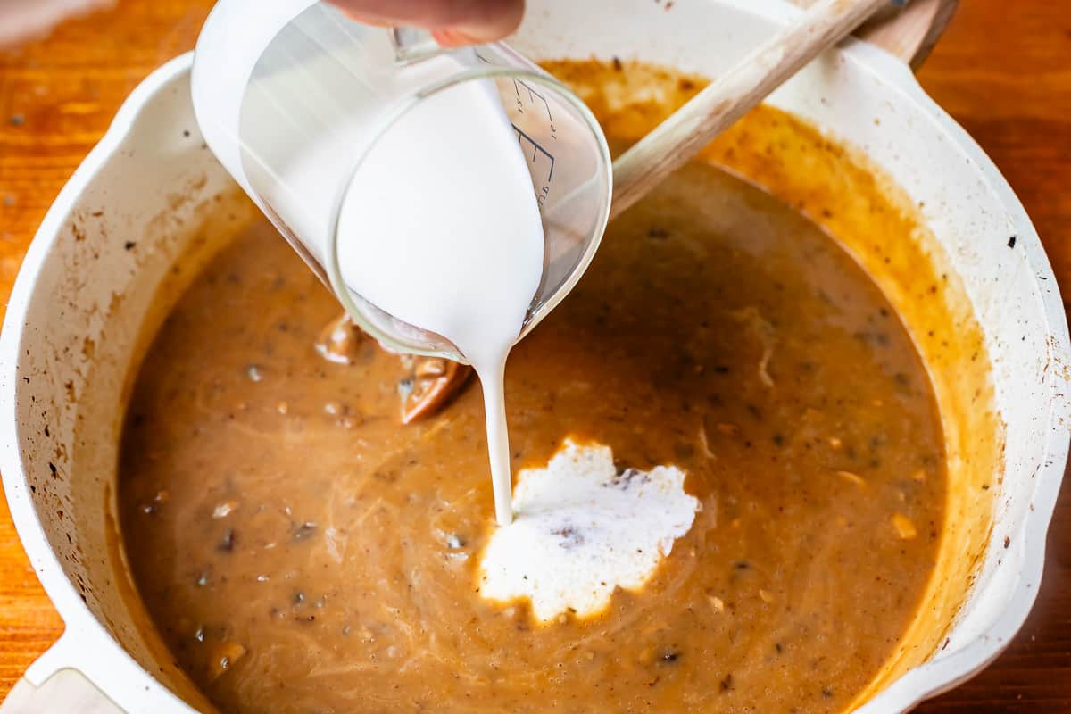 a glass measuring cup pouring cream into the gravy to make it creamy.
