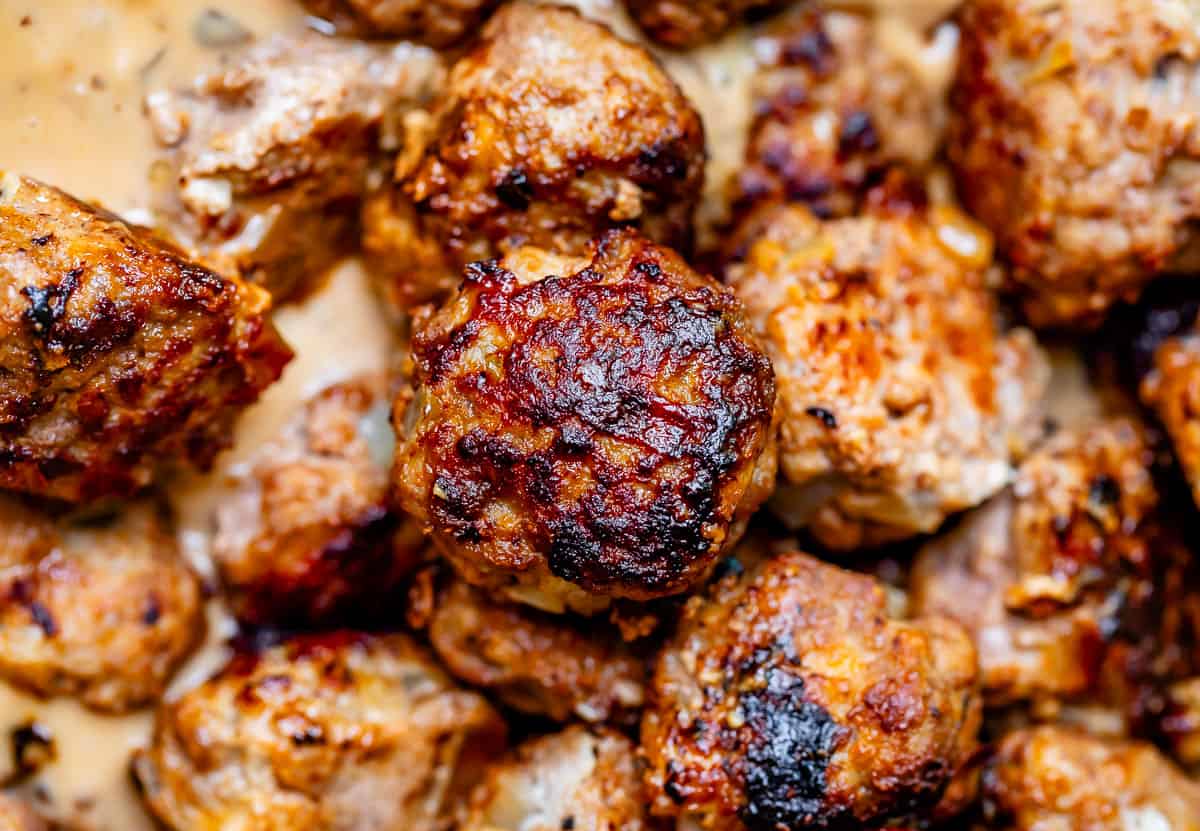 close up shot of a golden brown fried meatball with more cooked meatballs in the background.
