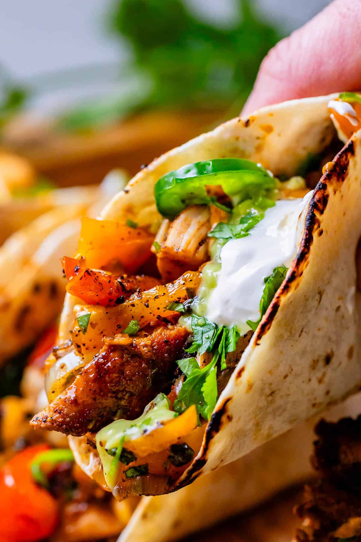 a hand holding a chicken fajita stuffed tortilla, with sour cream and jalapeno on top.