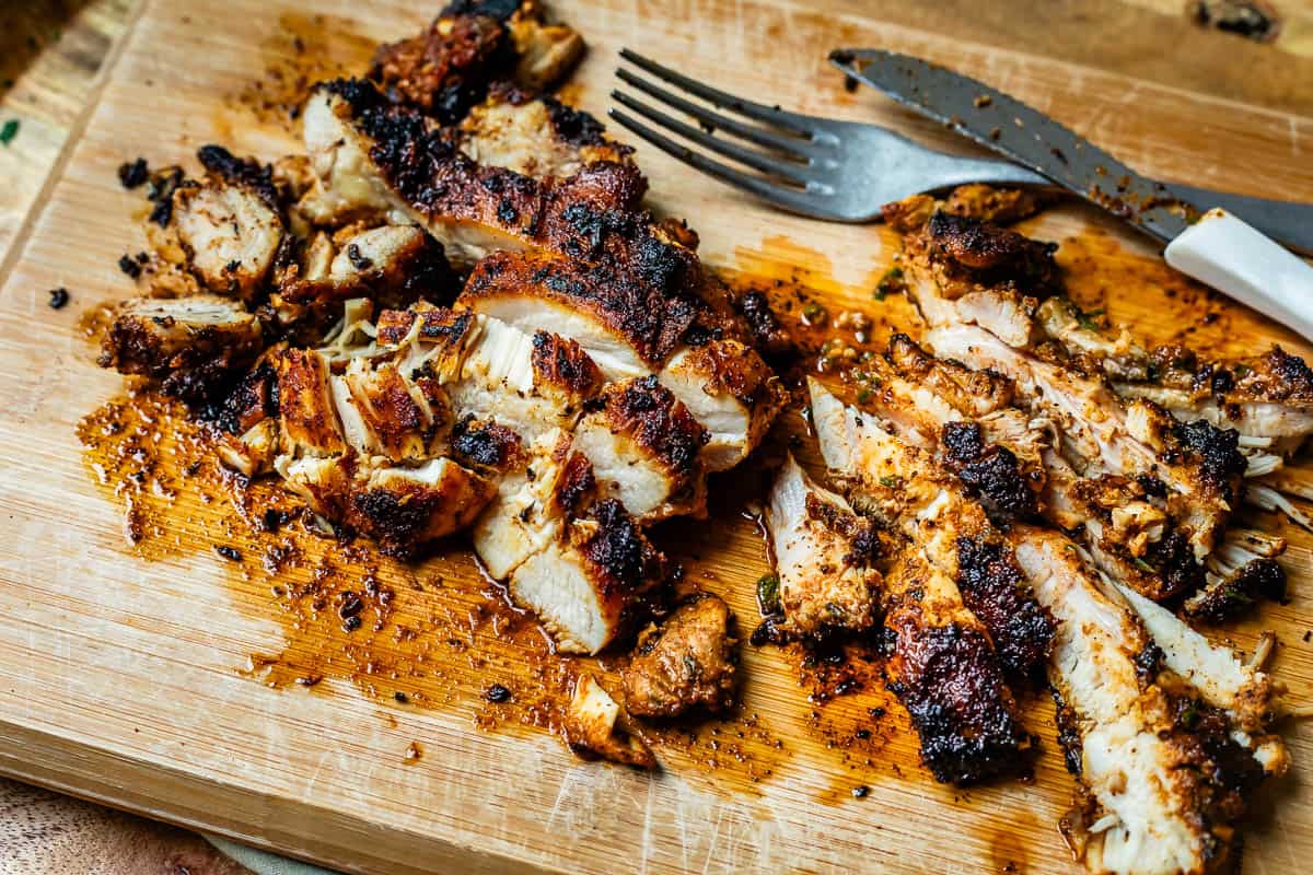 freshly sliced cooked chicken fajita breast with a fork and knife on a wooden cutting board.