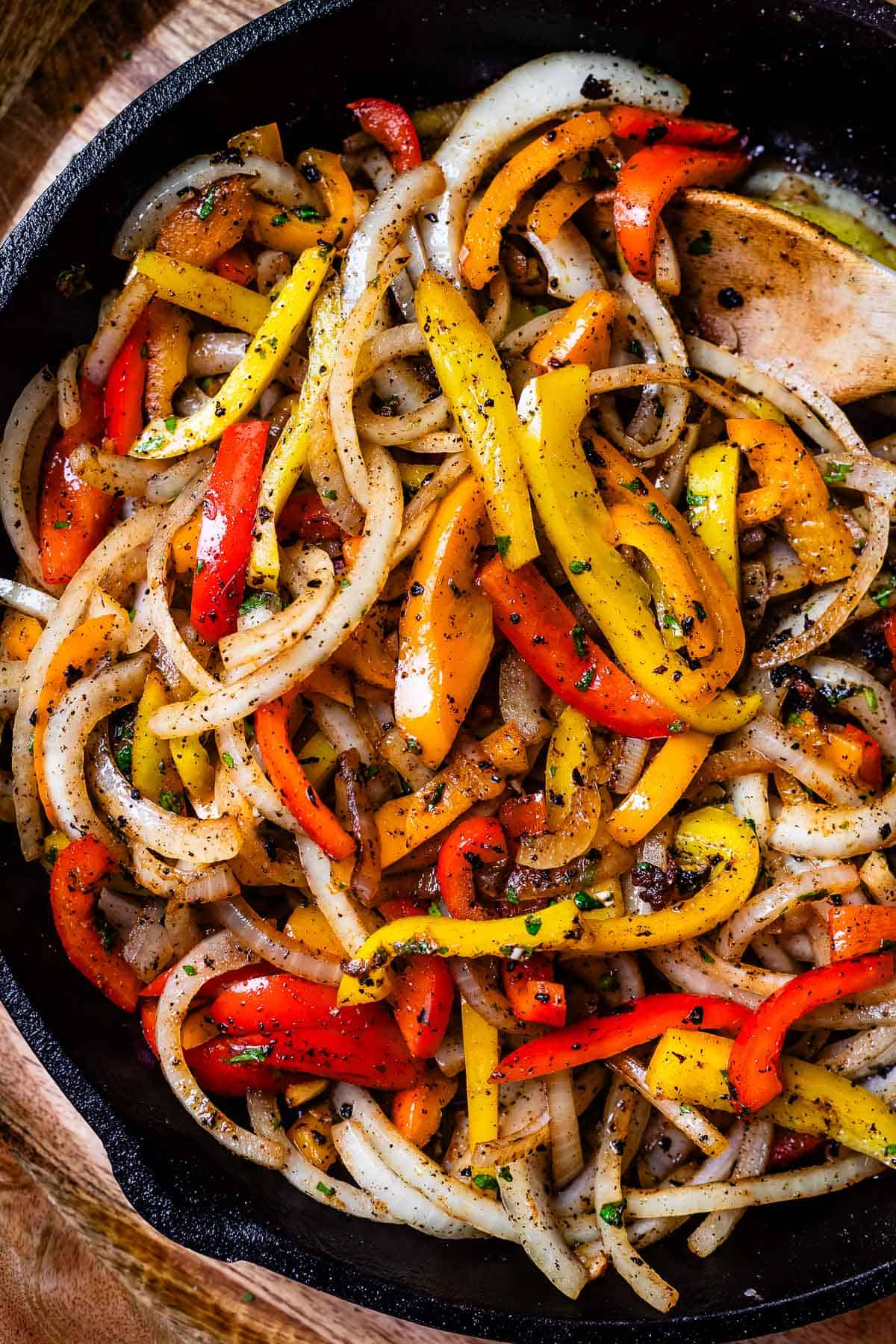 looking down into a cast iron skillet filled with sliced bell pepper and onion in marinade.