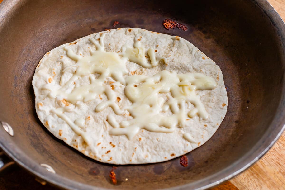 tortilla with melted white cheese in a dark skillet.