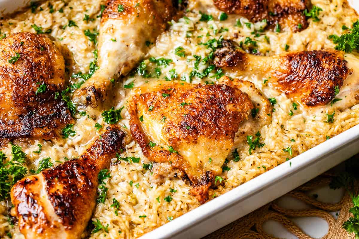seared chicken pieces in a casserole dish surrounded by creamy cooked rice.
