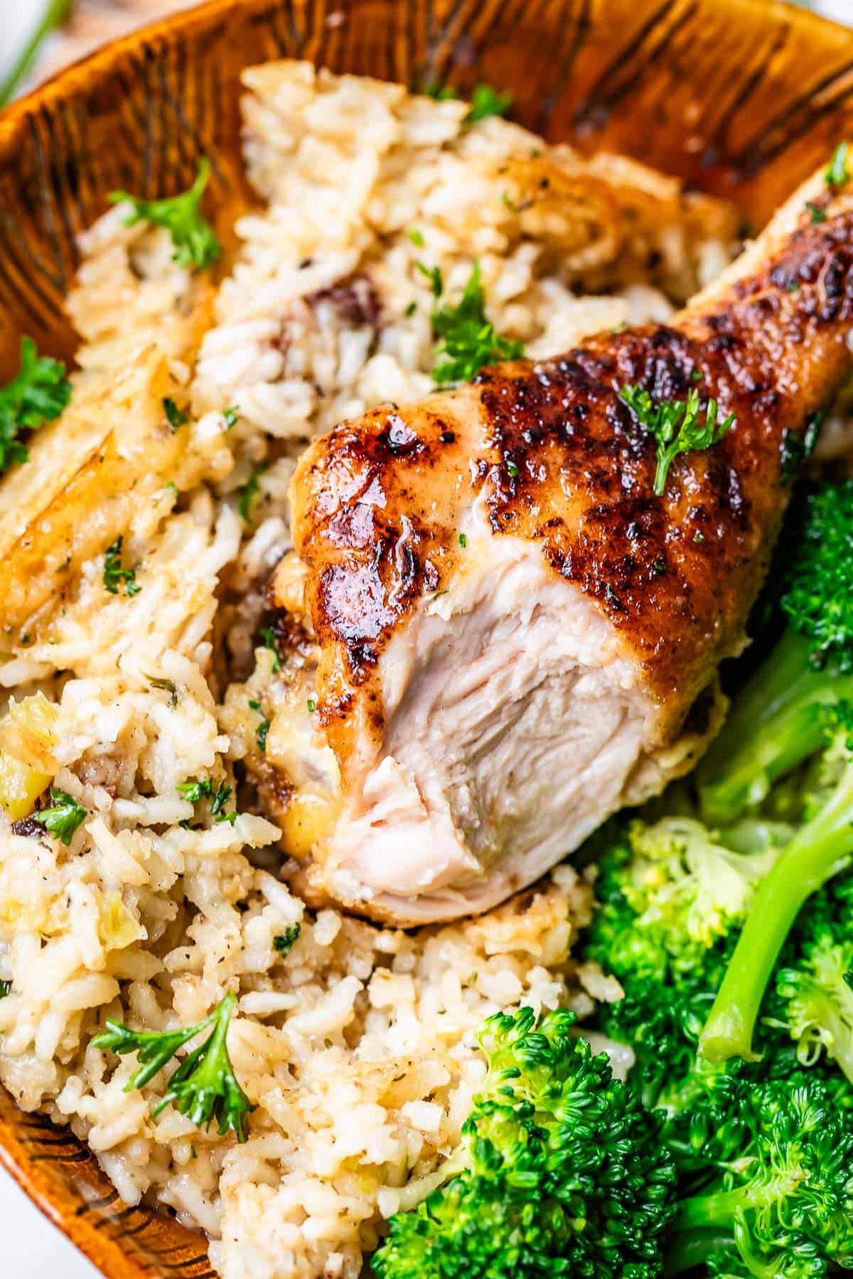 rice, broccoli, and chicken drumstick with bite taken out of it a wooden bowl.