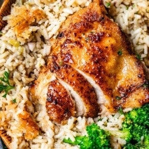 sliced chicken thigh in a bed of rice with broccoli in a wooden bowl.