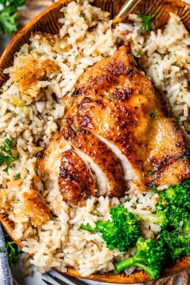 sliced chicken thigh in a bed of rice with broccoli in a wooden bowl.