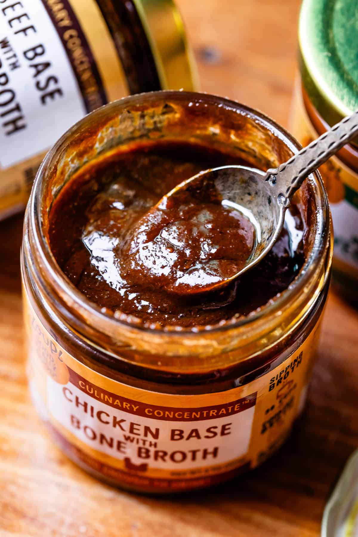 a spoon dipping into a jar of chicken broth base on a table.