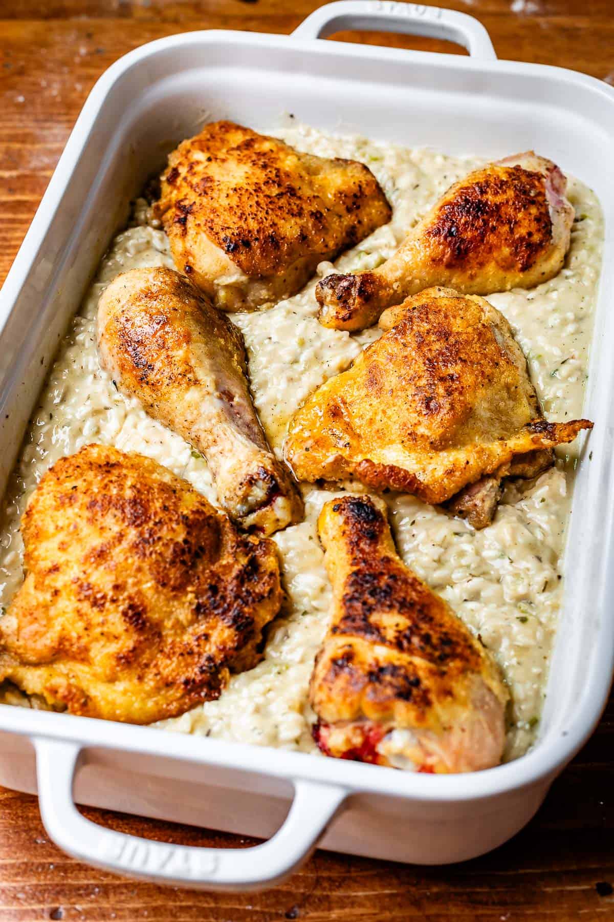 seared chicken pieces nestled into a rice and white sauce/water mix in a casserole dish.