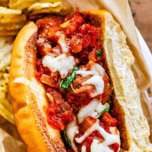 A delicious meatball sub topped with melted cheese and tomato sauce on a toasted bun, served with potato chips on the side.