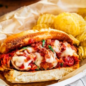 ready to eat meatball sub and potato chips served together on parchment paper in an oval plastic bowl.