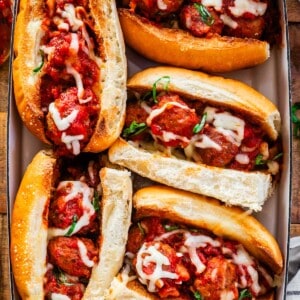 toasted hoagies stuffed with meatballs and sauce and covered in cheese in a baking dish.