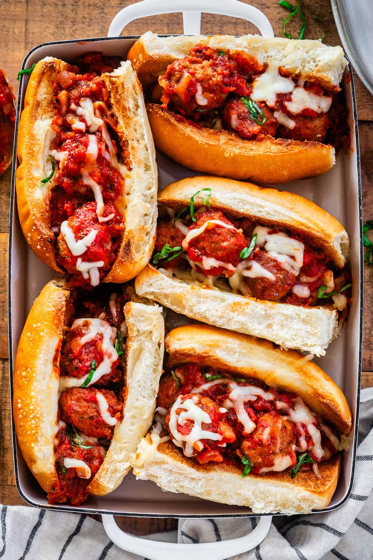 toasted hoagies stuffed with meatballs and sauce and covered in cheese in a baking dish.