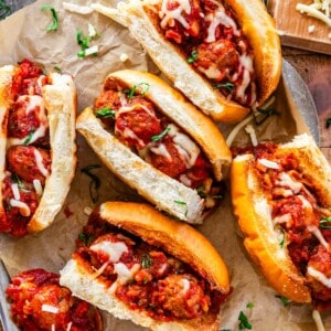 fully assembled meatball subs on parchment paper on a metal serving tray.