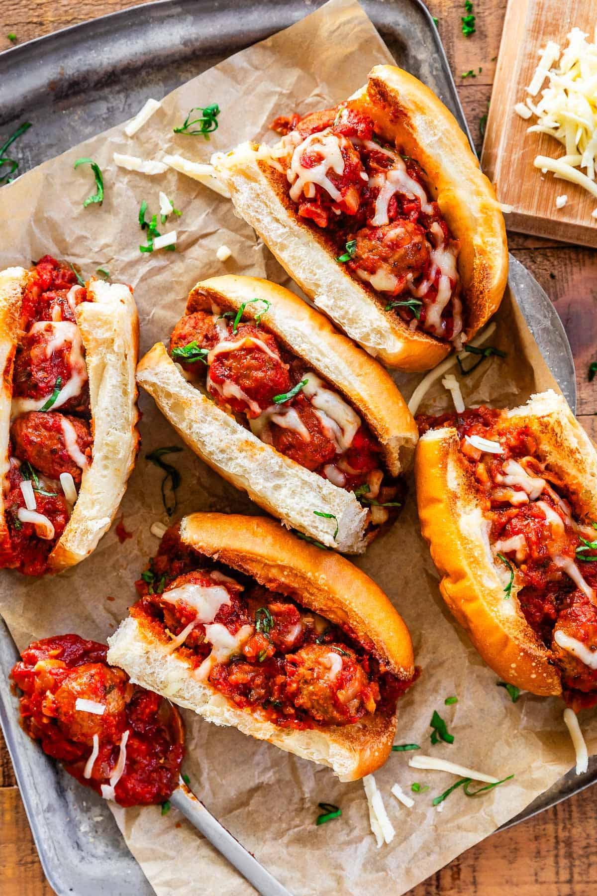 fully assembled meatball subs on parchment paper on a metal serving tray.