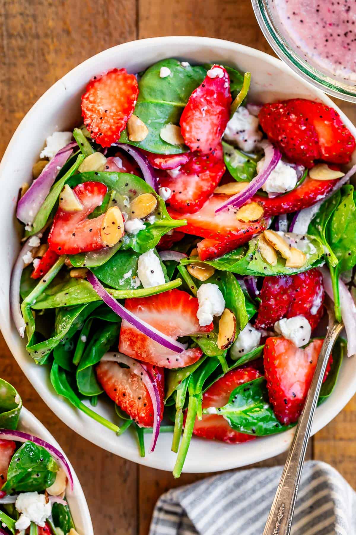 individual bowl filled to the top with dressed strawberry spinach salad with a spoon in it.