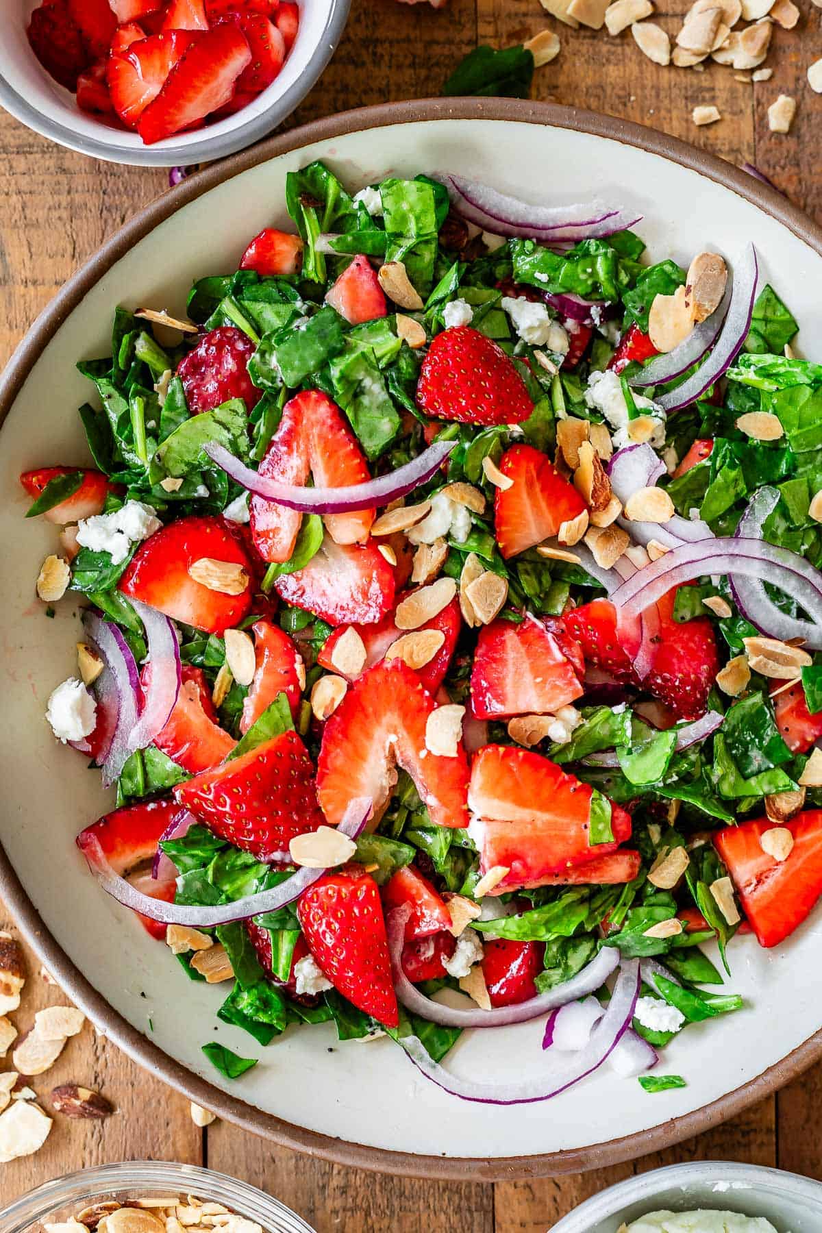 bowl filled with chopped spinach, strawberries, onions, goat cheese, and almonds.