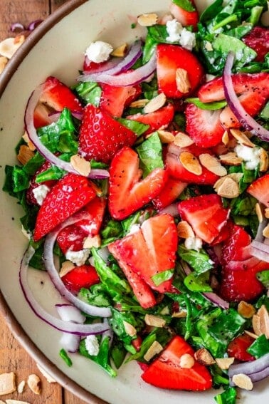 up close on half of a bowl filled with chopped spinach strawberry salad with poppyseed dressing.