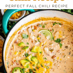 A pot of creamy white chicken chili garnished with sliced jalapeños, shredded cheese, and diced avocado, surrounded by fresh ingredients. Text reads, White Chicken Chili Recipe – the ultimate white chicken chili for fall.